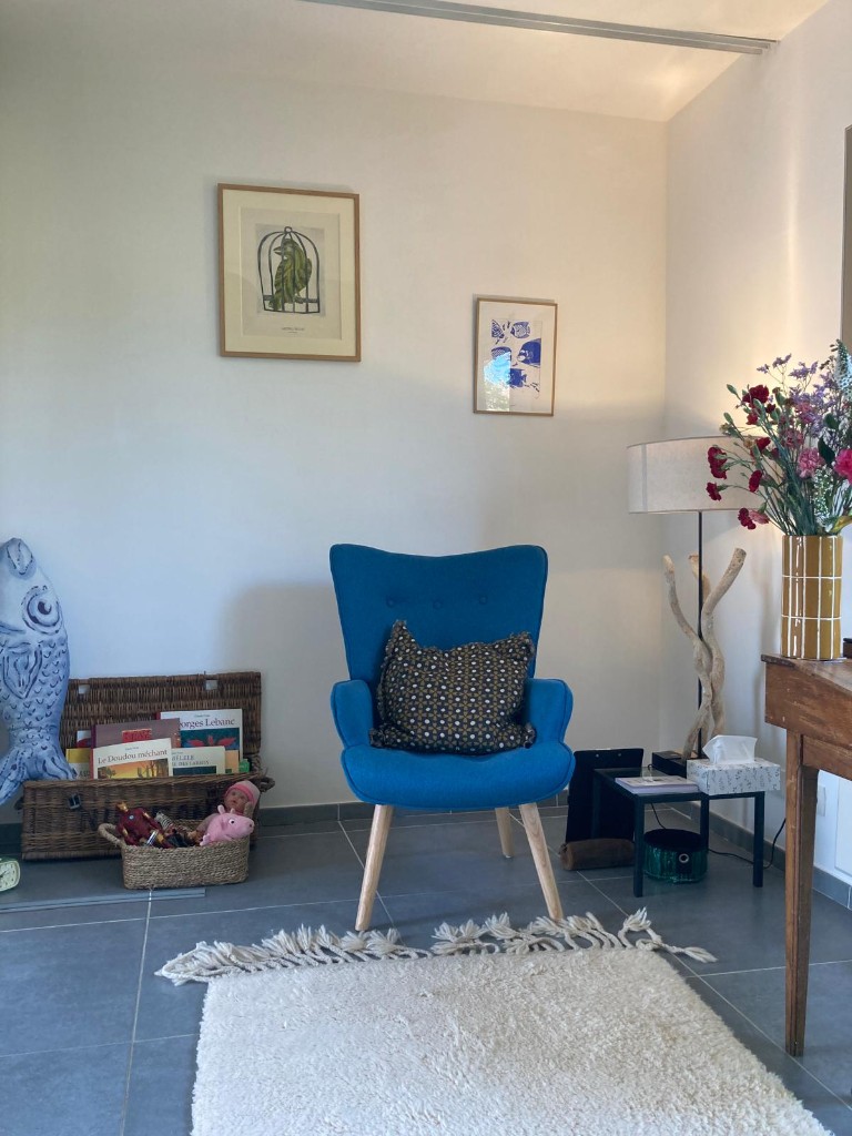 Espace d’accueil avec fauteuil bleu turquoise, coin livres et jeux pour les enfants